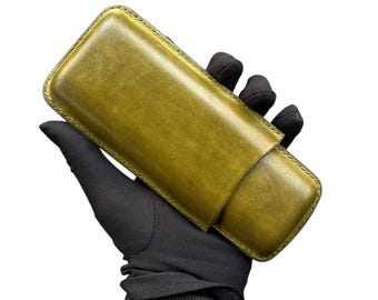 Puede incluir: Un estuche para cigarros de cuero verde con cierre de solapa. El estuche está hecho de cuero de alta calidad y tiene un acabado liso.