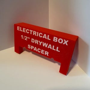 May include: A red plastic spacer for electrical boxes, labeled "ELECTRICAL BOX 1/2" DRYWALL SPACER".
