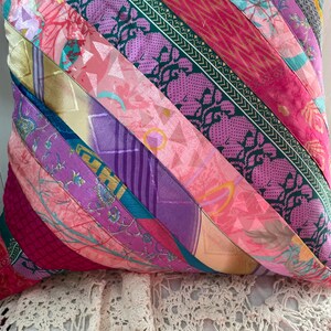 May include: A colourful pillow cover made from strips of fabric in shades of pink, purple, teal, and green. The fabric has a variety of patterns, including floral, geometric, and paisley.