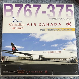 May include: A rectangular box for a 1/400 scale model airplane featuring the text B767-375 TRANSITIONAL LIVERY, Canadian Airlines, and Air Canada. The box displays a white airplane with a red maple leaf on the tail against a blue sky.