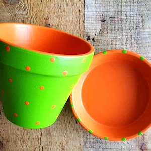 Medium painted polka dot planter in custom color combinations. Hand-painted terracotta flower pot with matching saucer, sealed for indoor or outdoor plants. Shown in orange and green.