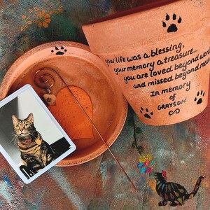 Personalized pet memorial planter with custom name and message.
Hand painted terracotta pet loss planter with matching saucer shown in orange.