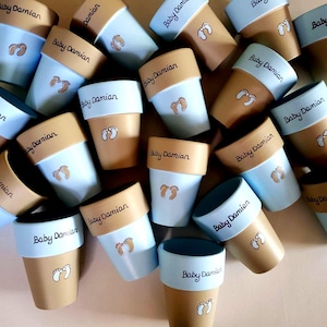 May include: A collection of small, decorative flower pots in shades of tan and light blue. Each pot is personalized with the name "Baby Damian" and a pair of baby footprints. The pots are arranged in a scattered pattern.