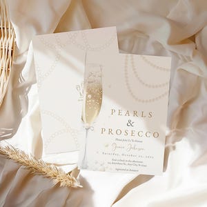 May include: A white invitation card with gold lettering that reads "Pearls & Prosecco". The invitation is for a party on Saturday, October 29, 2021, for Grace Johnson. The card is decorated with a pearl necklace and a glass of champagne.