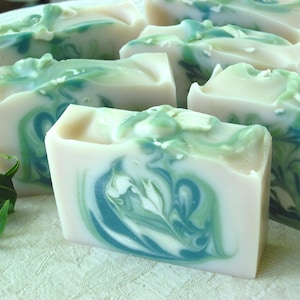 May include: A collection of handmade soap bars with a swirling green and white pattern. The soap bars are arranged on a white surface.