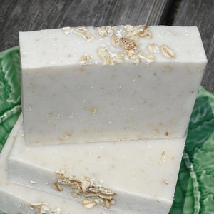 May include: Three bars of white soap with oatmeal flakes on a green plate. The soap is stacked on top of each other.