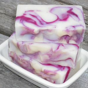 May include: A stack of three handmade soap bars with a white base and swirls of purple and pink.