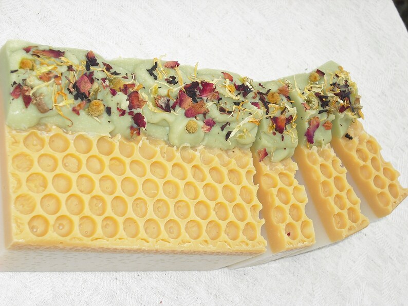 May include: A bar of handmade soap with a green layer on top and a yellow honeycomb pattern on the bottom. The green layer is decorated with dried flowers and herbs.