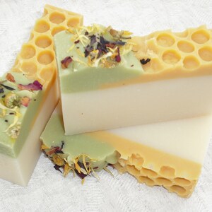 May include: Three bars of handmade soap with a honeycomb design, green and white layers, and dried flowers on top.