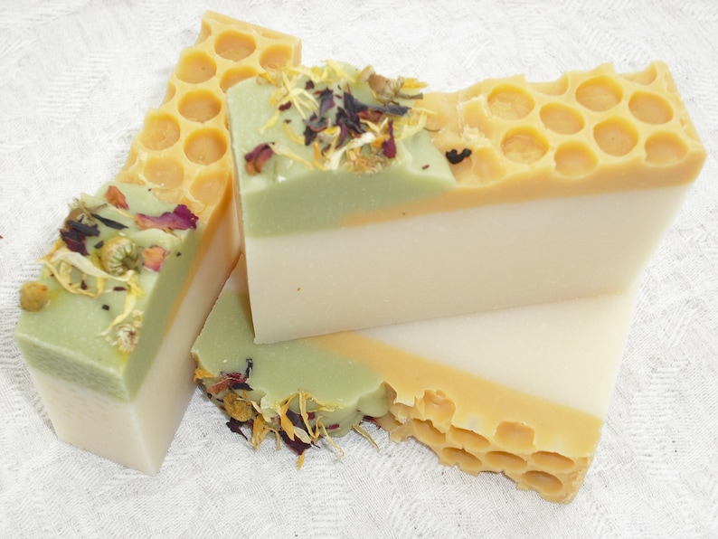May include: Three bars of handmade soap with a honeycomb design, green and white layers, and dried flowers on top.