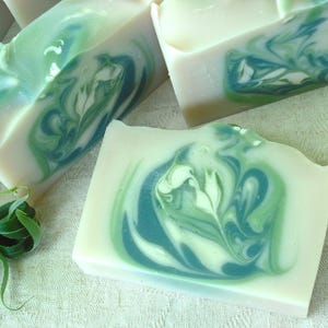 May include: Four bars of handmade soap with a swirl pattern of green and white. The soap is on a white surface with green leaves.
