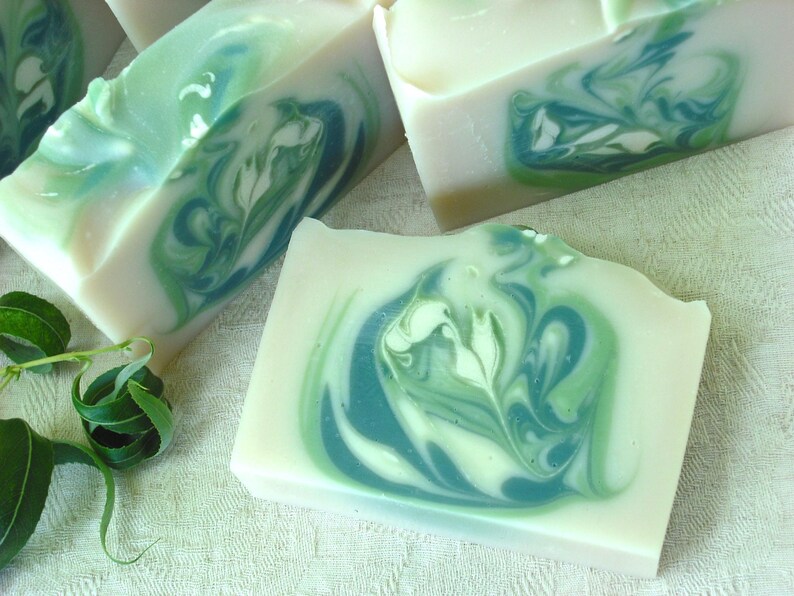 May include: Four bars of handmade soap with a swirl pattern of green and white. The soap is on a white surface with green leaves.