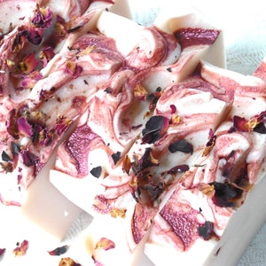 May include: Four bars of handmade soap with a swirl design in shades of white and pink. The soap is decorated with dried rose petals.