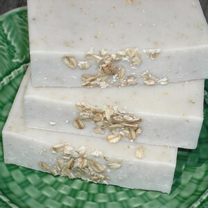 May include: Three bars of white soap with oatmeal flakes on top, sitting on a green plate.