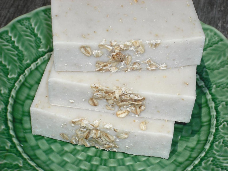 May include: Three bars of white soap with oatmeal flakes on top, sitting on a green plate.