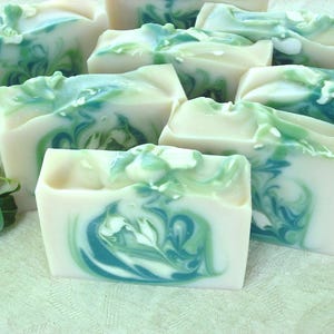 May include: A collection of handmade soap bars with a swirling green and white pattern. The soap bars are arranged on a white surface.