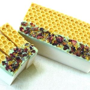 May include: Rectangular bars of soap featuring a yellow honeycomb-textured top layer, a light green middle section, and a white base. The top is decorated with a line of dried red rose petals, yellow calendula, and purple lavender flower buds.