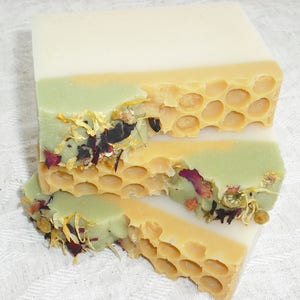May include: Three layers of handmade soap with a honeycomb design and dried flowers. The top layer is white, the middle layer is green, and the bottom layer is yellow.