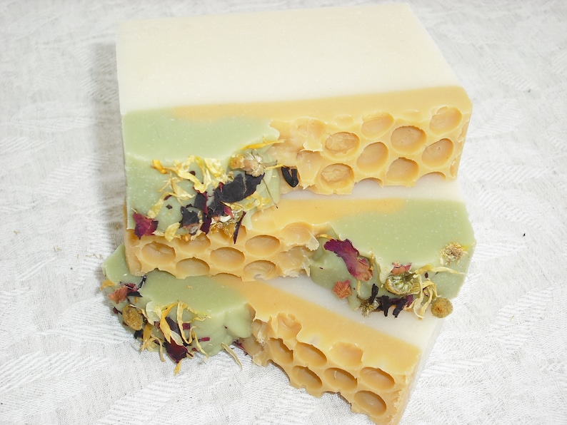 May include: Three layers of handmade soap with a honeycomb design and dried flowers. The top layer is white, the middle layer is green, and the bottom layer is yellow.