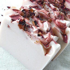 May include: A bar of white soap with swirls of pink and red, decorated with dried rose petals.