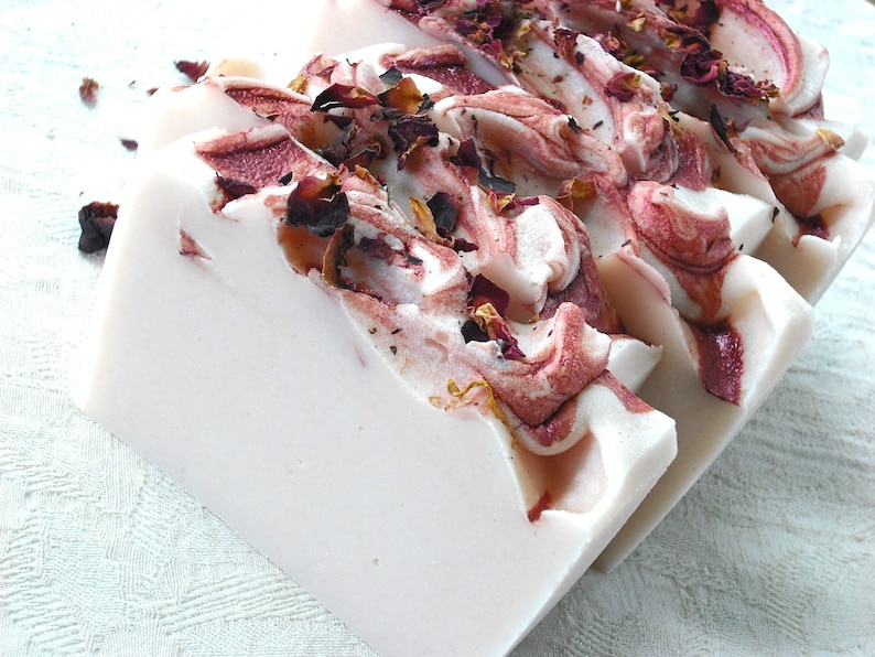 May include: A bar of white soap with swirls of pink and red, decorated with dried rose petals.