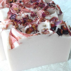 May include: A bar of handmade soap with a swirl design in shades of pink and white. The soap is decorated with dried rose petals.