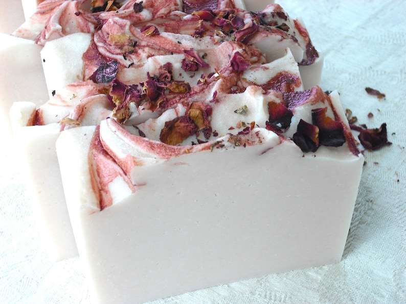 May include: A bar of handmade soap with a swirl design in shades of pink and white. The soap is decorated with dried rose petals.