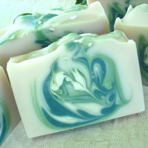 May include: Four bars of handmade soap with a swirling green and white pattern. The soap is made with natural ingredients and is perfect for sensitive skin.