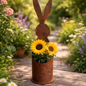 May include: A rustic metal rabbit silhouette planter with two bright yellow sunflowers. The planter has a cylindrical base and is set on a wooden walkway in a garden setting. The rabbit's ears extend upwards.