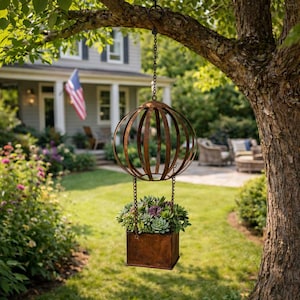 Puede incluir: Una jardinera colgante de metal con un diseño de jaula esférica y una jardinera rectangular. La jardinera está suspendida de una cadena y llena de suculentas verdes y moradas. El metal tiene un aspecto rústico y desgastado, añadiendo un toque de encanto vintage a la decoración exterior.