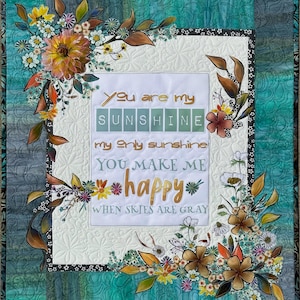 May include: A quilted wall hanging with a floral design and the text "You are my sunshine." The quilt features a white center with the text, surrounded by colorful flowers and leaves. The background is a mix of teal and gray.