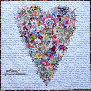 May include: A white fabric heart-shaped quilt with a floral design. The quilt is decorated with various flowers, including pink, red, blue, and yellow. The quilt also features the text "Start each day with a grateful heart" and "Amazing love".
