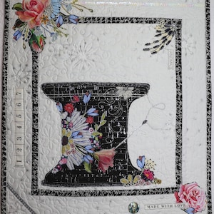 May include: A white fabric square with a black and white sewing machine design in the center. The design is surrounded by a black border and a white border. The fabric is quilted with a floral pattern. The words "HANDMADE" and "MADE WITH LOVE" are written on the fabric.