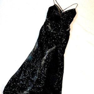 May include: A black, floor-length evening gown with a V-neckline and spaghetti straps. The dress is covered in sparkling embellishments, creating a shimmering effect. The fabric appears to be velvet or a similar material.