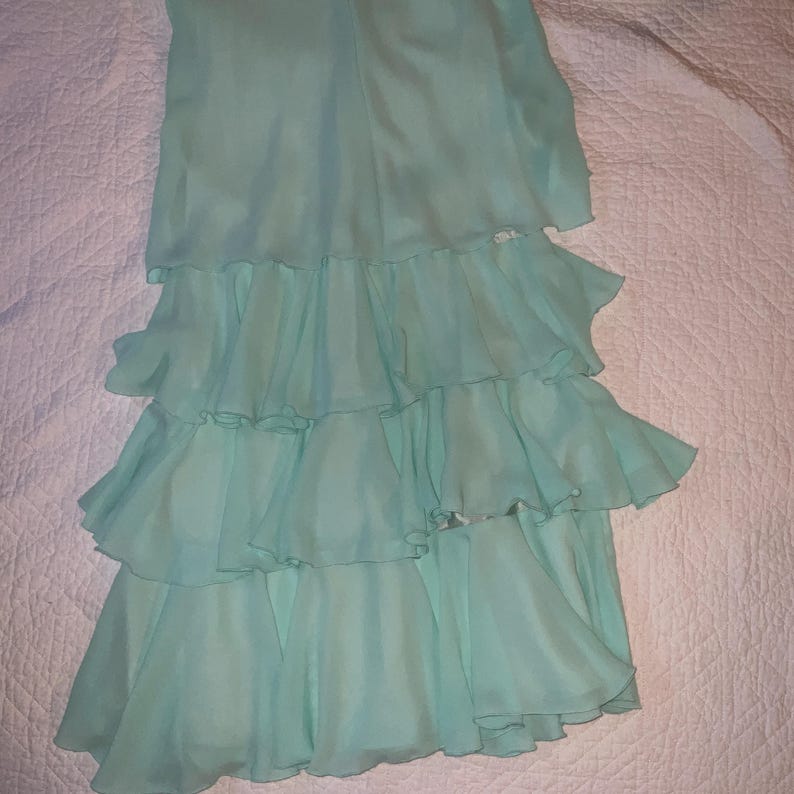 May include: A light blue, tiered dress with a flowing, ruffled design. The dress features multiple layers of soft fabric, creating a cascading effect. The dress is made of a lightweight material, perfect for warm weather.
