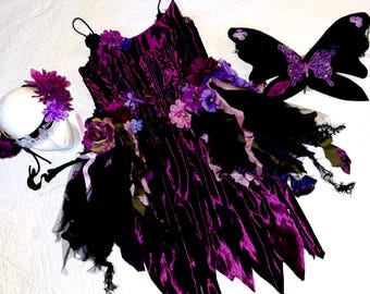 May include: A fairy costume set featuring a deep purple dress with black accents, floral embellishments, and delicate straps. The set includes matching black butterfly wings and a floral headband, all on a white background.