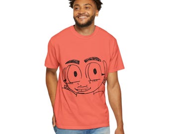 May include: Coral-colored t-shirt featuring a black cartoon face design. The graphic has large eyes, a small nose, and a smiling mouth. The shirt is made of a soft material and has short sleeves.