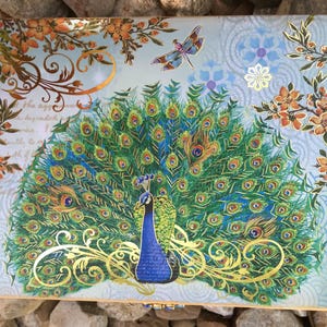 A gift box featuring a peacock with a fanned tail, showcasing shades of green, blue, and gold. The design includes ornate gold embellishments. The box is rectangular. Luxury Natural Perfume Gift Set: Floral Aromatherapy - Sovereign Collection