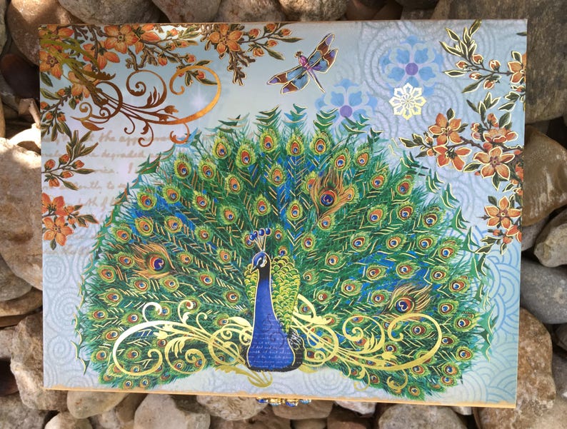 A gift box featuring a peacock with a fanned tail, showcasing shades of green, blue, and gold. The design includes ornate gold embellishments. The box is rectangular. Luxury Natural Perfume Gift Set: Floral Aromatherapy - Sovereign Collection