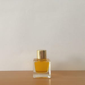 A 6 ml square perfume bottle with a gold cap. The bottle is filled with a yellow  parfum which is named Divine Love natural perfume. The bottle is sitting on a wooden surface, with a white background.