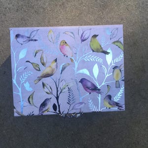 A rectangular silver foil gift box with a light background and a pattern of colorful birds perched on silver-colored branches. The birds are various colors, including yellow, purple, and pink. The box has a silver-colored brooch clasp.
