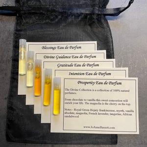 May include: A collection of perfume samples in small glass vials, each containing a different colored liquid. The vials are arranged on white cards with the names of the perfumes printed on them. The cards are inside a black drawstring bag.