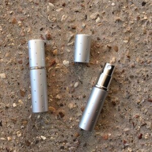 Silver perfume atomizer with a removable cap and a spray nozzle. The atomizer has a cylindrical shape with small, evenly silver dots.  Luxury Natural Perfume Gift Set: Floral Aromatherapy - Sovereign Collection of JoAnne Bassett