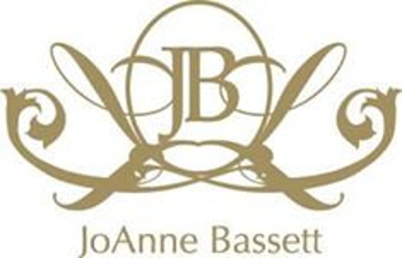 JoAnne Bassett Natural Perfumes gold-colored logo featuring the initials "JB" intertwined within an oval shape, with elegant, flowing lines and flourishes. The name "JoAnne Bassett" is written below in a serif font.