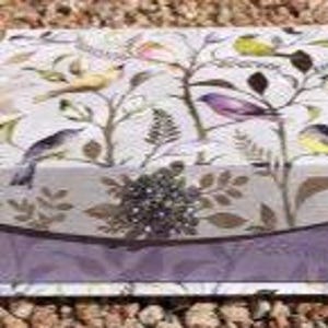 A decorative box with a lid. The box features a repeating pattern of colorful birds perched on branches with leaves, set against a light background. The box has a lavender border. Luxury Natural Perfume Gift Set, Sovereign Collection by JoAnne Bassett
