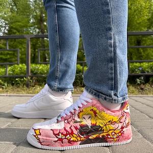 May include: White and pink custom sneakers with a character design. The sneakers feature a white base with pink accents and a detailed illustration of a character with yellow hair and red flames. A second pair of white sneakers is visible in the background.