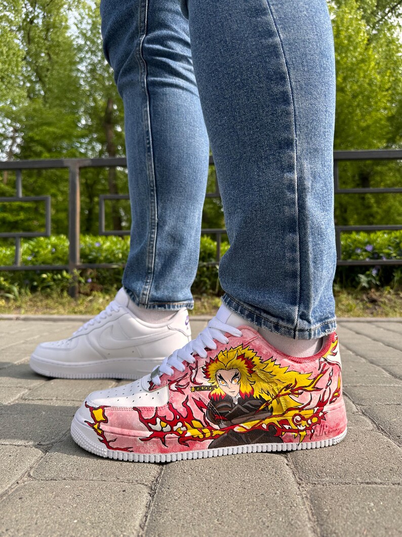 May include: White and pink custom sneakers with a character design. The sneakers feature a white base with pink accents and a detailed illustration of a character with yellow hair and red flames. A second pair of white sneakers is visible in the background.