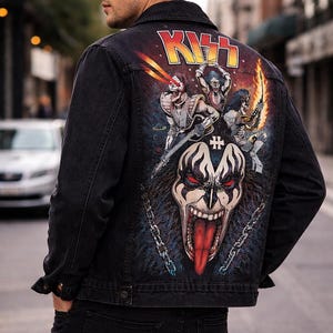 May include: Black denim jacket with a colorful graphic on the back featuring the band KISS. The artwork includes the band's logo, band members, and a large face with a red tongue. The jacket is worn by a person.