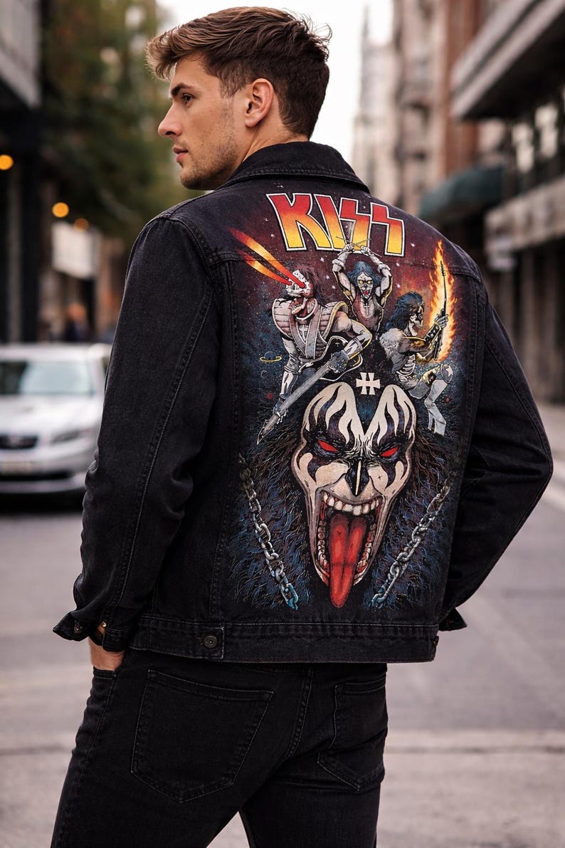 May include: Black denim jacket with a colorful graphic on the back featuring the band KISS. The artwork includes the band's logo, band members, and a large face with a red tongue. The jacket is worn by a person.