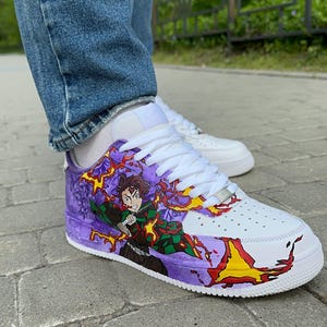 May include: White sneakers with custom artwork featuring a character in a green and black outfit with purple and yellow flames. The shoes have white laces and a purple and white design on the sides.